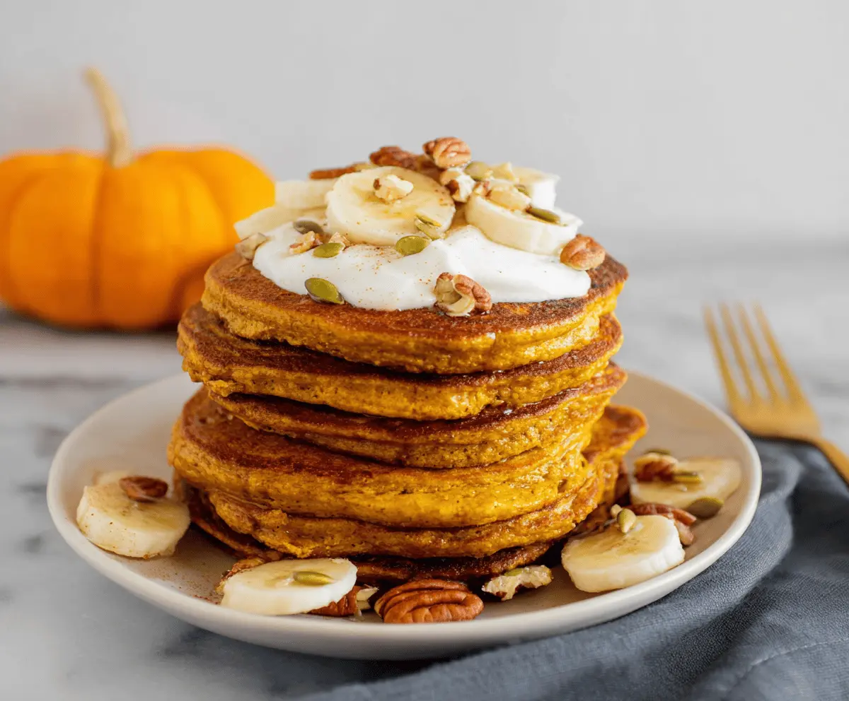 Delicious fluffy pumpkin protein pancakes topped with maple syrup and fresh cinnamon, perfect for a healthy breakfast.