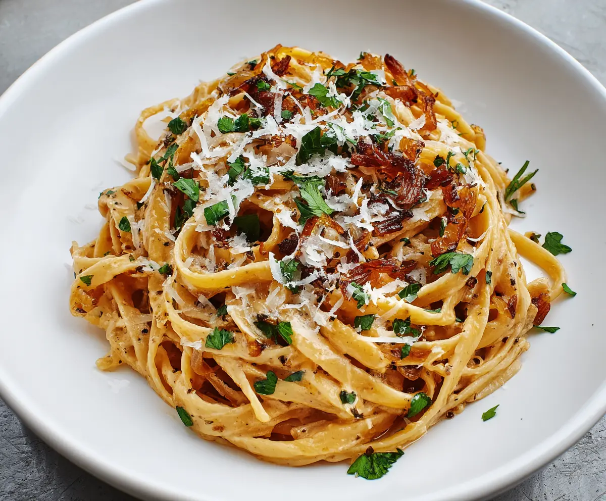 Delicious caramelized onion pasta served on a white plate with a sprinkle of herbs.