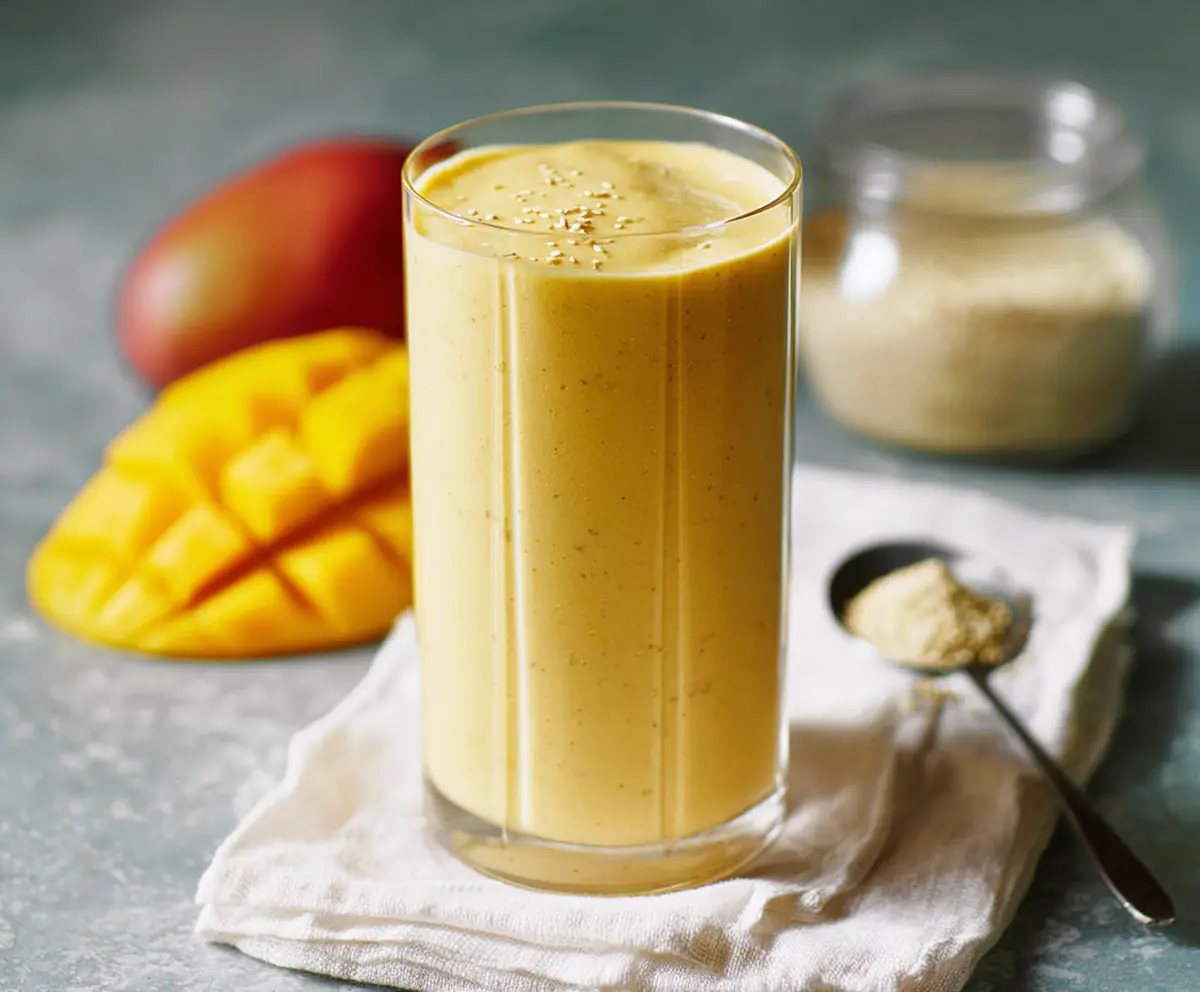 Refreshing Mango Protein Smoothie in a glass with a straw, garnished with fresh mango slices and mint leaves.