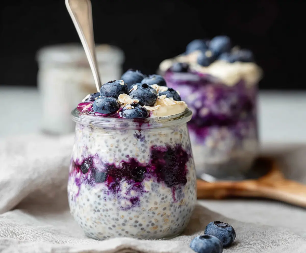 Creamy blueberry cheesecake overnight oats topped with fresh blueberries and a graham cracker crumb crust.