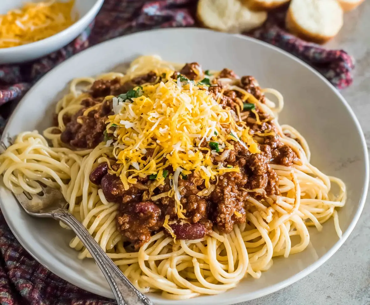 Delicious Cincinnati Chili Spaghetti served in a bowl topped with shredded cheese and chopped onions.