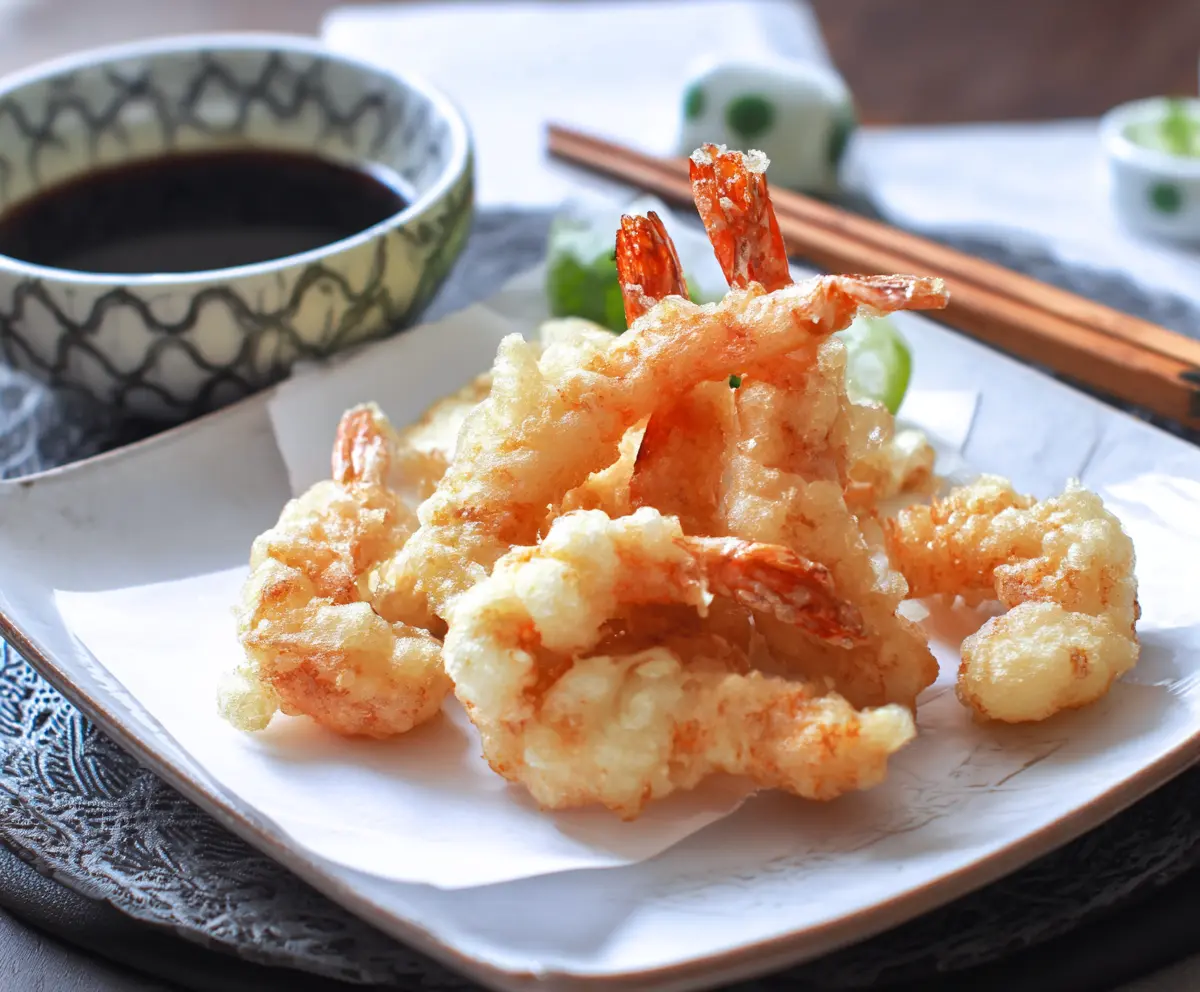 Crispy Japanese shrimp tempura served with dipping sauce on a plate.