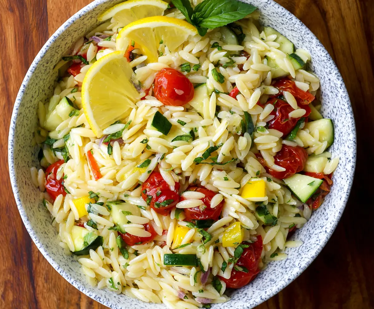 Fresh Lemon Orzo Pasta Salad with herbs and vegetables on a white plate.