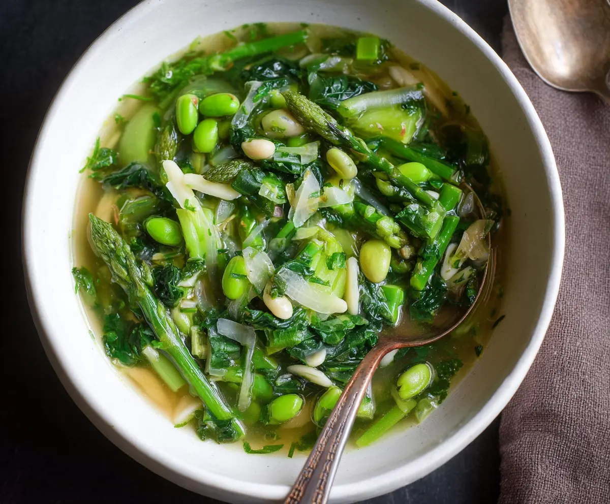 A bowl of vibrant spring green minestrone soup with fresh vegetables and herbs.