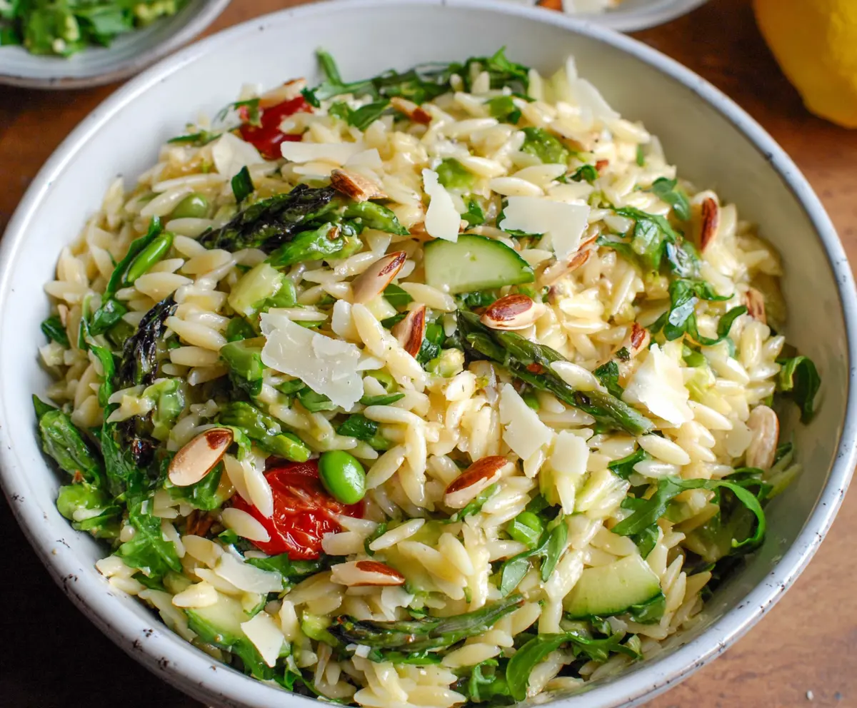 Colorful spring orzo pasta salad with fresh vegetables and herbs on a white plate.
