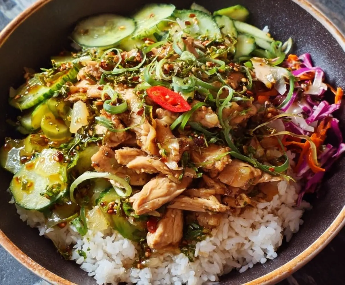 Ginger scallion chicken bowl with fresh herbs and vegetables on a white plate.